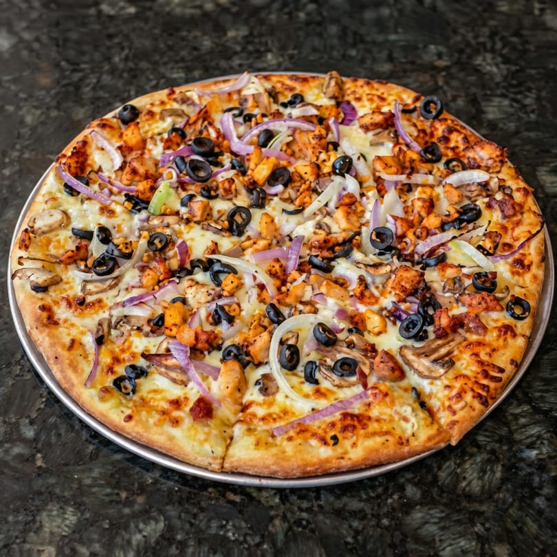 A whole chicken, mushroom, olive, and onion pizza on a dark granite surface.