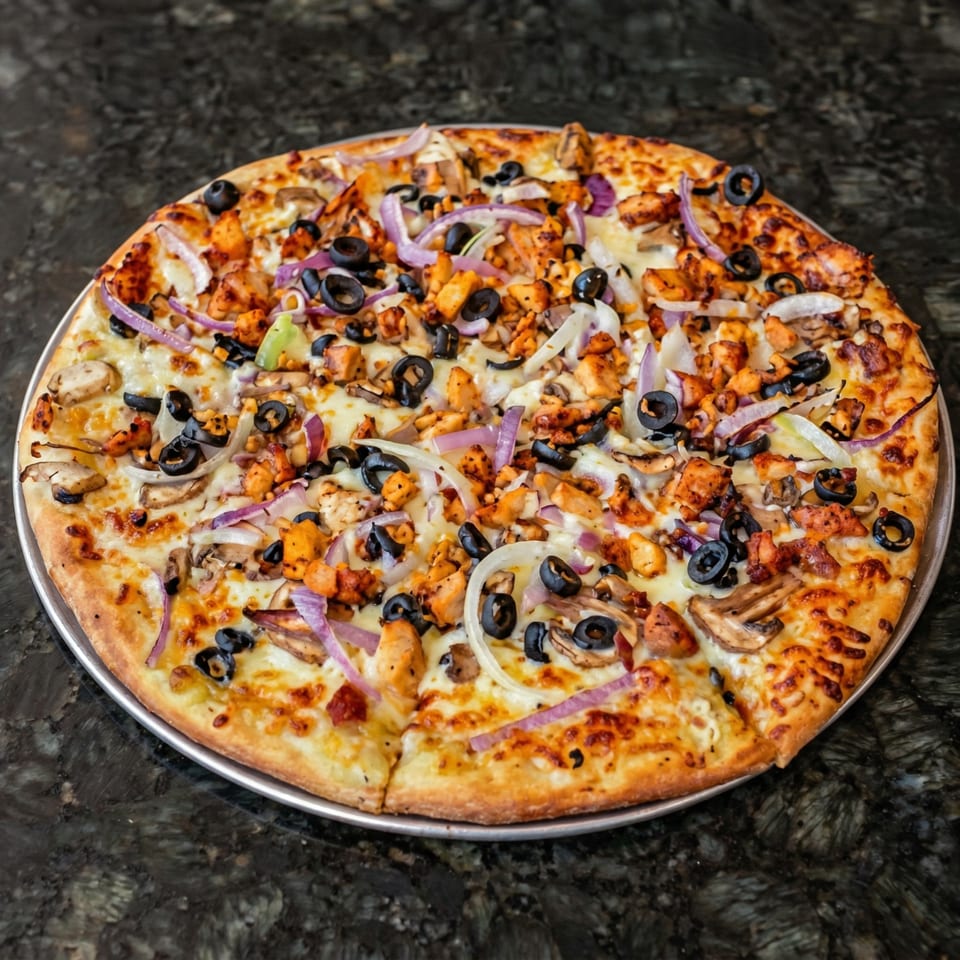 A whole pizza with chicken, black olives, red onions, and mushrooms on a dark countertop.