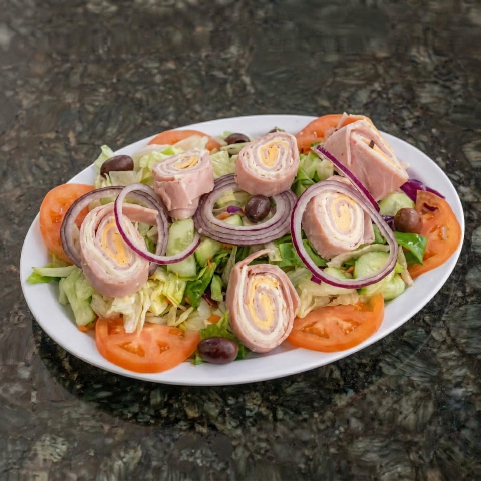 Chef salad with ham and cheese rolls, lettuce, tomatoes, red onions, cucumbers, and olives.