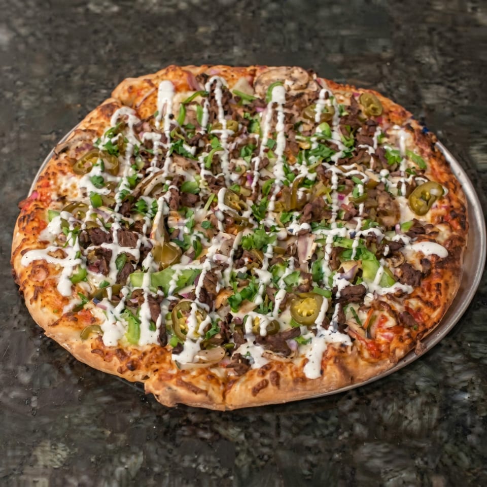 A large pizza topped with beef, jalapenos, green peppers, and a white sauce drizzle.