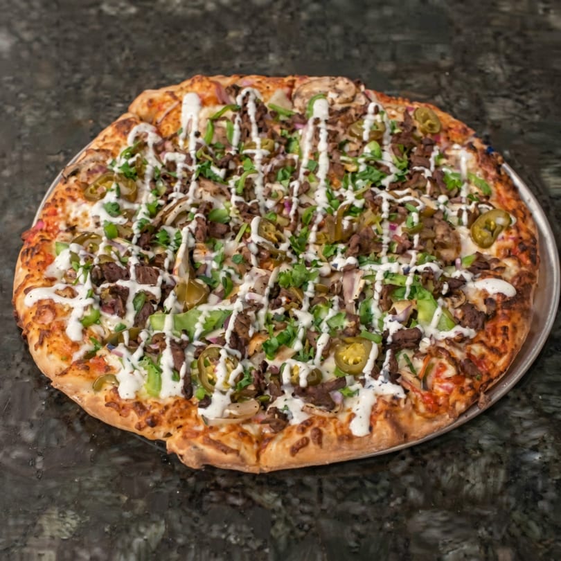 A large pizza topped with beef, jalapenos, green peppers, and a white sauce drizzle.